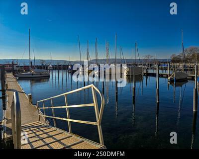 Einige Segelboote im Hafen Uberlingen in Deutschland, in der Wintersonne, bereit für eine neue Saison. Im Vordergrund - eine Spur zum Segeln und klares sauberes Wasser. Stockfoto