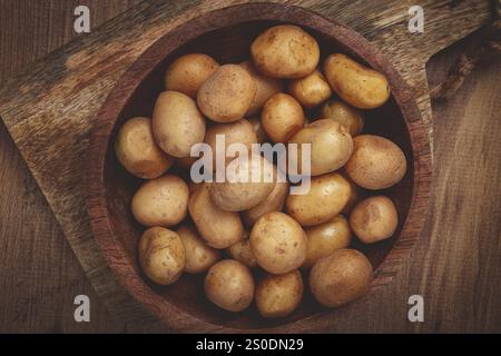 Eine Schüssel gefüllt mit frisch geernteten kleinen Kartoffeln zeigt ihre natürlichen Erdtöne. Die Holzoberfläche verleiht dem setti Wärme und rustikalen Charme Stockfoto