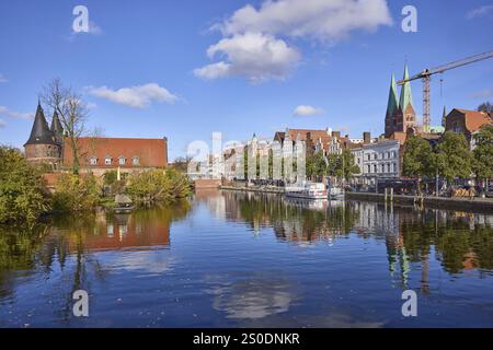 River Trave, Holsten Gate, historische Salzlager, Bäume, allgemeine Architektur, Kirchturm von St. Mary's, blauer Himmel mit Schönwetterwolken, Ref Stockfoto