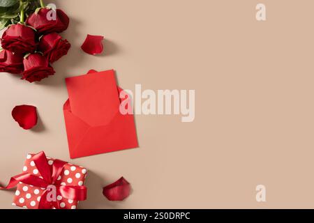 Valentinskarte mit leerem Liebesbrief, roten Rosenblüten und rotem Umschlag, Geschenk auf beigefarbenem Hintergrund. Blick von oben. Kopierbereich. Stockfoto