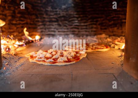 Frische Pizzas, die im Holzofen einer rustikalen Pizzeria gebacken werden Stockfoto