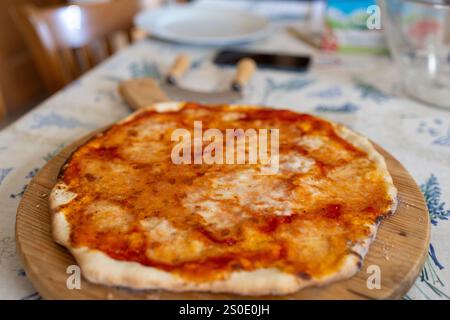 Eine Nahaufnahme einer frisch gebackenen hausgemachten Pizza mit Tomatensauce und geschmolzenem Käse, präsentiert auf einer rustikalen Holzserviertafel. Stockfoto