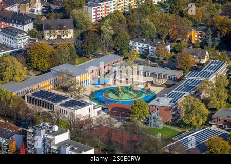 Vogelperspektive, Kolibri-Schule Grundschule und Kreiszentrum H2Ö, farbenfrohe kreisförmige Inneneinrichtung und Spielplatz mit Bäumen auf dem Schulhof, Stockfoto