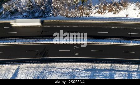 Eine Top-down-Perspektive auf eine Autobahn, umgeben von schneebedecktem Gelände, mit fahrenden Lkw. Stockfoto