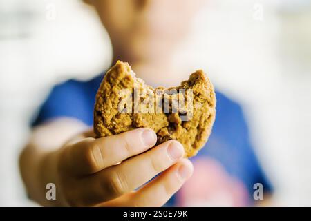 Ein Kind hält einen Keks in der Hand, und ein Biss wird daraus entfernt. Das Konzept der Unschuld und des Genusses, da das Kind eine süße Leckerei genießt Stockfoto