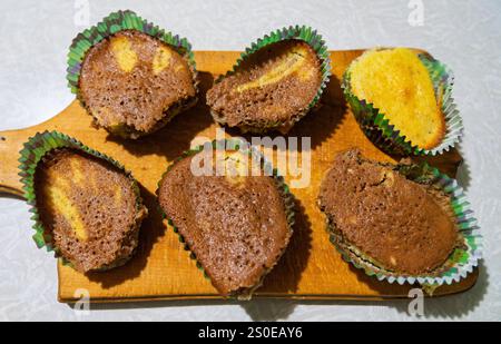 Sechs leckere Kuchenscheiben, etwas Schokolade und etwas Vanille, werden auf ein Holzbrett gelegt. Das Küchenambiente verleiht dem reizvollen Display Wärme Stockfoto