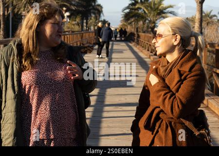 Zwei Frauen führen ein lebhaftes Gespräch, während sie auf einem Holzsteg spazieren. Stockfoto