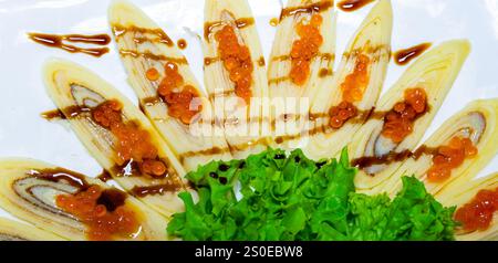 Eine wunderschön angeordnete Sushi-Platte zeigt dünn geschnittenen frischen Fisch, mit Sauce bespritzt und mit hellem Orangenfischrogen belegt, begleitet von einem B Stockfoto