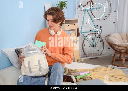 Männlicher Student, der Rucksack im Schlafzimmer packt Stockfoto