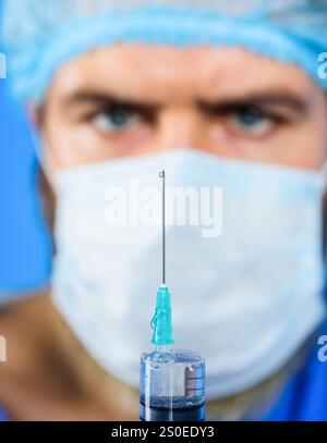 Männlicher Arzt in chirurgischer Maske, der Spritze mit Nadel für die Injektion vorbereitet. Impfungen für Menschen. Arzt in Uniform hält Spritze mit Impfstoff. Dok Stockfoto