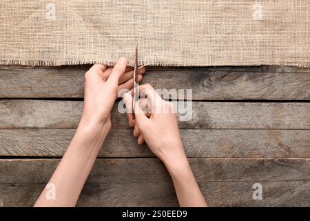 Frau schneidet Sackleinen auf hölzernem Hintergrund Stockfoto