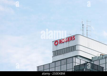 Burnaby, KANADA - 2. August 2024 : Top of a Rogers Building mit Kommunikationsantennen und einem markanten roten Logo vor einem klaren blauen Himmel. Stockfoto