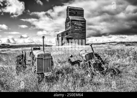 Zwei alte Traktoren sitzen auf einem Feld neben einem Kornsilo. Die Szene ist ruhig und friedlich, mit dem einzigen Knarren der alten Maschine Stockfoto