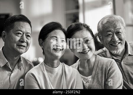 Schwarz-weiß-Porträt zweier glücklicher älterer asiatischer Paare, die die Kamera lächelnd betrachten Stockfoto