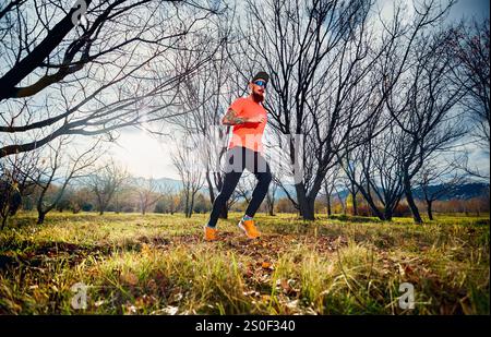 Sportlicher bärtiger Mann in rotem Hemd, der bei Sonnenaufgang im Herbstwald auf dem Wanderweg läuft Stockfoto