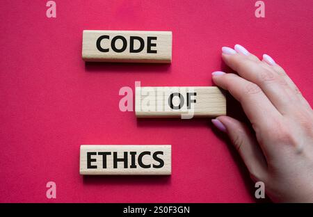 Symbol für Ethikkodex. Konzeptworte Ethik-Kodex auf Holzblöcken. Schöner roter Hintergrund. Geschäftsmann Hand. Business und Ethik-Konzept. Stockfoto