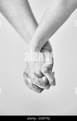 Zwei Hände in der Hand vor neutralem Hintergrund gehalten. Nahaufnahme der Hand von Mann und Frau. Konzept von Intimität, Unterstützung und Vertrauen. Schwarzweißbild. Stockfoto