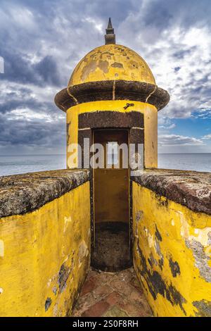 Lebendiger Wachturm aus gelbem Stein entlang der Küste mit malerischem Blick auf das Meer unter flauschigen Wolken. Stockfoto