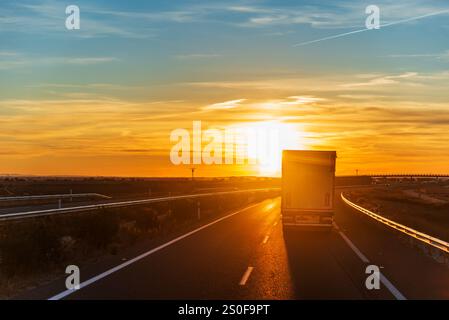 Ein Lkw fährt über eine Autobahn, während die Sonne am Horizont untergeht und der Nacht Platz macht, ein anspruchsvoller Job unter atemberaubender Aussicht. Stockfoto