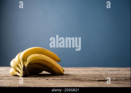 Ein frischer Haufen reifer, gelber Bananen auf einem Holztisch, mit einem minimalistischen blauen Hintergrund, der die Komposition unterstreicht. Mit einem Kopierraum auf der r Stockfoto