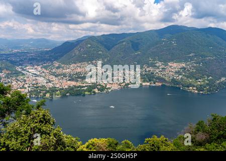 Panoramablick auf eine malerische Stadt am See, umgeben von üppigen grünen Bergen und ruhigem Wasser, mit Booten, die unter teilweise bewölktem Wasser auf dem See segeln Stockfoto