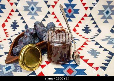 Pflüstern Sie Marmelade oder Marmelade mit violetten Pflaumen auf einem Vorhang mit ethnischen Mustern Stockfoto