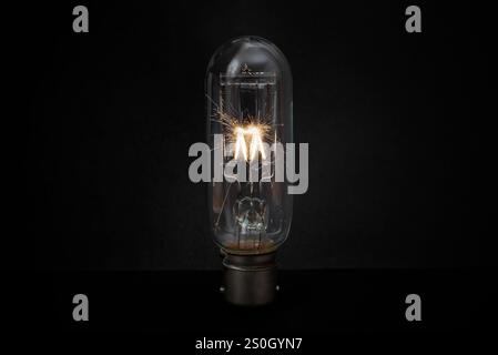 Nahaufnahme einer beleuchteten antiken Film- oder Projektionslampe mit hohem Lichtstrom und explodierendem Glühfaden mit orangefarbenen Funken, ovaler kleiner Glühbirne Stockfoto