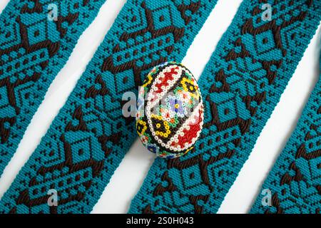 Rumänisches perlenbesetztes Ei, osterdekoration auf blauem Textilrand Streifen Hintergrund Stockfoto