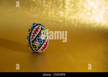 Rumänisches perlenbesetztes Ei, osterdekoration auf defokussiertem goldenen Glitzer-Hintergrund, Kopierraum Stockfoto