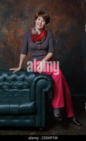 Eine Frau mittleren Alters saß auf der Rückseite des Sofas auf braunem Hintergrund Stockfoto