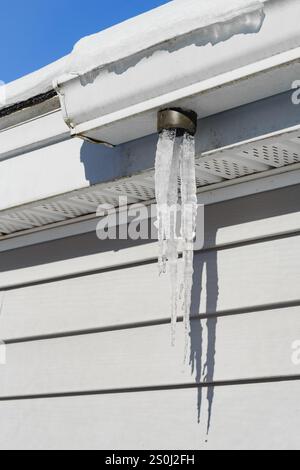 Eiszapfen tropfen im Winter aus einer gefrorenen Hausrinne Stockfoto