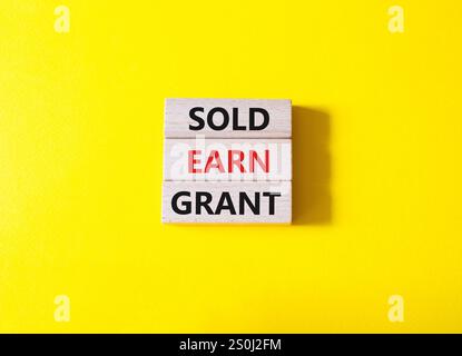 Symbol „Sold Earn Grant“. Verkaufte Konzeptworte verdienen Grant auf Holzblöcke. Schöner gelber Hintergrund. Business und Sold Earn Grant Concept. Kopierbereich. Stockfoto