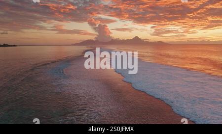 Meereswellen sanft rollende Sandküste der tropischen Insel Tahiti bei Sonnenuntergang. Leuchtende orange Farben und dramatische Wolken, die sich im Wasser spiegeln. Abgelegenes wildes Naturparadies, exotische Sommerreise. Luftaufnahme Stockfoto