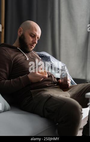 Schlafender betrunkener Mann, der auf dem Sofa einschläft und eine Flasche Whiskey und Glas in den Händen hält. Traurigkeit. Ermüdung. Kopierbereich Stockfoto