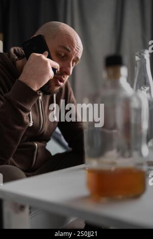 Der betrunkene Mann hält das Telefon in der Hand und redet. Bekämpfung der Depression. Alkoholismus. Kopierbereich Stockfoto
