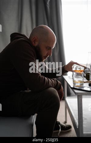 Gesundheitswesen. Alkoholismus, betrunkener, müder Europäer, der eine Flasche Whisky in der Hand hält, einsam deprimierter Mann, der Alkohol auf dem Sofa trinkt. Behandlung Stockfoto