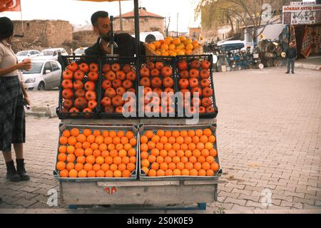 Derinkuyu, Nevşehir, Türkei - 23. November 2024 : Ein Mann, der frische Orangen und Granatäpfel auf einem mobilen Wagen auf einem Marktplatz verkauft Stockfoto