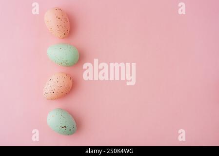 Vier Eier in verschiedenen Pastellfarben sind in einer Reihe auf rosafarbenem Hintergrund angeordnet. Die Eier sind mit einem gesprenkelten Muster bemalt, Osterkonzept. Stockfoto