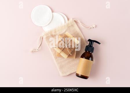Eine Kollektion natürlicher Pflegeprodukte auf sanftem rosafarbenem Hintergrund. Enthält eine Pumpflasche, handgefertigte Seife und wiederverwendbare Wattepads in einem Stockfoto