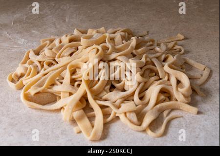 Haufen handgemachter Fettuccini-Nudeln auf bemehlter Oberfläche Stockfoto