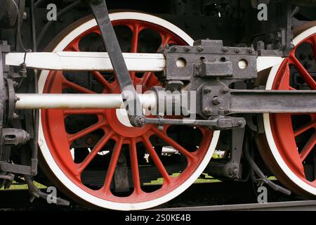 Detaillierte Nahaufnahme der leuchtenden roten Speichenräder und der komplizierten mechanischen Komponenten eines alten Zuges, die Präzision und Histoire festhalten Stockfoto