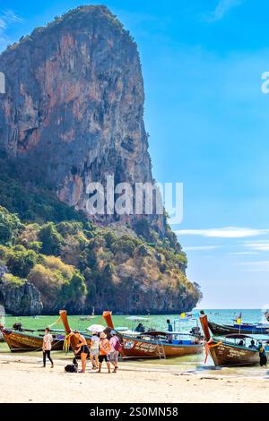 Touristen kommen am Railay Beach auf Langboot-Booten an, die in einer Meeresbucht vor dem Hintergrund der Bergklippen in der Provinz Krabi, Thailand-03.17.2024, verankert sind Stockfoto