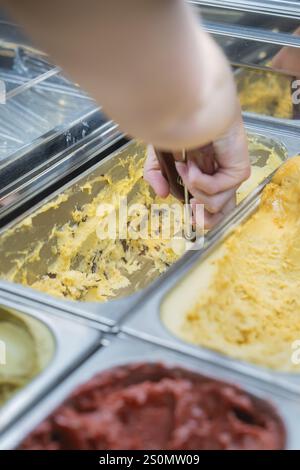 Eine Hand schöpft gelbes Eis aus einer Metallbox mit einem Eislöffel, Herbstkreationen im Cafe Kuh, Deckenpfronn, Deutschland, Europa Stockfoto