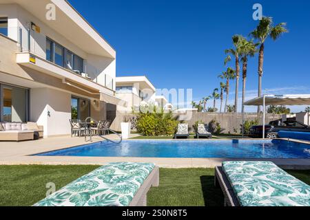 Moderne Villa in Vistabella, Spanien, mit privatem Pool, üppigem Garten, Liegestühlen und Palmen unter klarem Himmel. Stockfoto