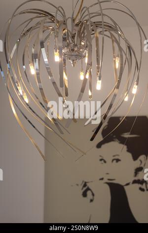 Nahaufnahme eines modernen Kronleuchters mit metallischen Kurven und LED-Leuchten, mit abstraktem Porträt im Hintergrund. Stockfoto