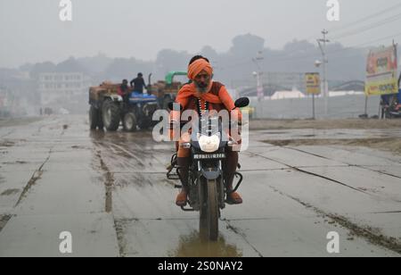 PRAYAGRAJ, INDIEN - 28. DEZEMBER: Ein Sadhu, der bei Regen in Mahakumbh Nagar am 28. Dezember 2024 in Prayagraj, Indien, ein Motorrad fährt. Die nächste Maha Kumbh Mela findet vom 13. Januar bis 26. Februar 2025 in Prayagraj statt. Das Festival wird voraussichtlich über 400 Millionen Pilger anziehen. Quelle: SIPA USA/Alamy Live News Stockfoto