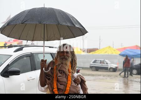 PRAYAGRAJ, INDIEN - 28. DEZEMBER: Ein Sadhu mit einem Regenschirm bei Regen am Mahakumbh Nagar am 28. Dezember 2024 in Prayagraj, Indien. Die nächste Maha Kumbh Mela findet vom 13. Januar bis 26. Februar 2025 in Prayagraj statt. Das Festival wird voraussichtlich über 400 Millionen Pilger anziehen. Quelle: SIPA USA/Alamy Live News Stockfoto