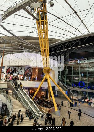 Innenansicht der O2 Arena, einem belebten, modernen Einkaufszentrum mit einzigartigem architektonischen Design und Menschen, die um die Rolltreppen und Geschäfte laufen Stockfoto