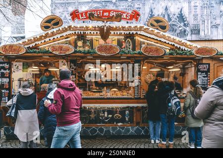Straßburg, Frankreich - 6. Dezember 2024: Weihnachtsmärkte, an denen vor dem Straßburger Dom Lebensmittel verkauft werden, mit vielen Menschenmassen Stockfoto
