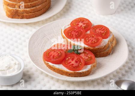Köstliche Sandwiches mit offenem Gesicht, belegt mit frischen Tomaten und Frischkäse, serviert auf einem strukturierten weißen Teller Stockfoto